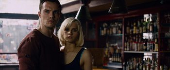 Movie still from “Collide” (2016), directed by Eran Creevy – A man and a woman posing for a picture in front of a bar; Close Up shot, Low angle