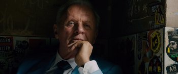 Movie still from “Collide” (2016), directed by Eran Creevy – An older man wearing a suit and tie with his hand under his chin; Close Up shot, Low angle