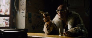 Movie still from “Collide” (2016), directed by Eran Creevy – A man in a fur coat holding a gun at a bar; Medium shot, Low angle