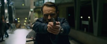 Movie still from “Collide” (2016), directed by Eran Creevy – A man holding a gun while wearing a jacket; Close Up shot, Low angle