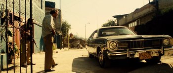 Movie still from “Colombiana” (2011), directed by Olivier Megaton – A man standing next to an old car on the side of the road; Wide shot, Low angle