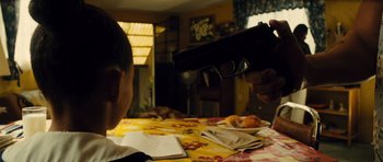Movie still from “Colombiana” (2011), directed by Olivier Megaton – A person holding a gun pointed at a table with food on it; Close Up shot, High angle