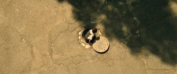 Movie still from “Colombiana” (2011), directed by Olivier Megaton – A man standing in a manhole on the street; Extreme Wide shot, Overhead angle