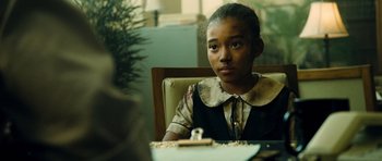 Movie still from “Colombiana” (2011), directed by Olivier Megaton – A young girl sitting at a table looking at the camera; Close Up shot, Over the shoulder angle