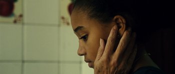 Movie still from “Colombiana” (2011), directed by Olivier Megaton – A woman with her hand on the ear of another person; Close Up shot, Over the shoulder angle