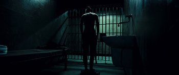 Movie still from “Colombiana” (2011), directed by Olivier Megaton – A man standing in a dark room next to a jail cell; Wide shot, Low angle