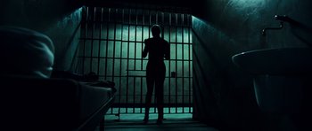 Movie still from “Colombiana” (2011), directed by Olivier Megaton – A person standing in a room with a cell phone; Wide shot, Low angle