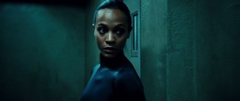 Movie still from “Colombiana” (2011), directed by Olivier Megaton – A woman standing in a room with a door in the background; Close Up shot, Low angle