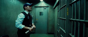 Movie still from “Colombiana” (2011), directed by Olivier Megaton – A man standing in front of a jail cell holding a cell phone; Medium shot, Low angle