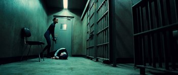 Movie still from “Colombiana” (2011), directed by Olivier Megaton – A man laying on the ground next to a door; Wide shot, Low angle
