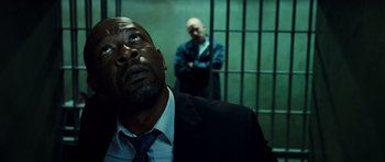 Movie still from “Colombiana” (2011), directed by Olivier Megaton – A man in a suit and tie standing next to another man in a jail cell; Close Up shot, Low angle