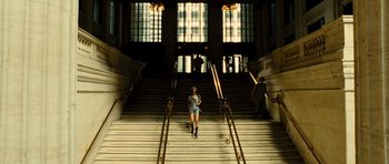 Movie still from “Colombiana” (2011), directed by Olivier Megaton – A woman is walking down some stairs in a building; Wide shot, Low angle