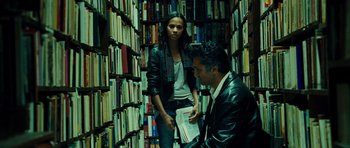 Movie still from “Colombiana” (2011), directed by Olivier Megaton – A man and a woman are standing in a room full of books; Medium shot, Low angle