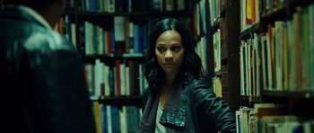 Movie still from “Colombiana” (2011), directed by Olivier Megaton – A woman standing in front of a book shelf in a library; Medium shot, Over the shoulder angle