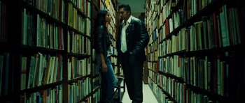 Movie still from “Colombiana” (2011), directed by Olivier Megaton – A man and a woman standing in front of a wall of books; Medium shot, Low angle