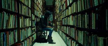Movie still from “Colombiana” (2011), directed by Olivier Megaton – A person sitting on a chair in a library; Wide shot, High angle