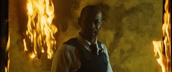 Movie still from “Colombiana” (2011), directed by Olivier Megaton – A man wearing a tie standing in front of a fire; Close Up shot, Low angle