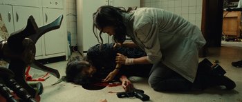 Movie still from “Colombiana” (2011), directed by Olivier Megaton – A woman helping a man who is lying on the ground; Medium shot, High angle