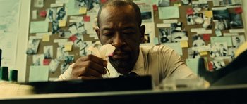Movie still from “Colombiana” (2011), directed by Olivier Megaton – A man sitting at a desk holding a flower in front of his face; Extreme Close Up shot, Over the shoulder angle