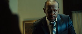 Movie still from “Colombiana” (2011), directed by Olivier Megaton – A man wearing a suit and tie in front of a painting; Close Up shot, Low angle