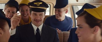 Movie still from “Colonia” (2015), directed by Florian Gallenberger – A man and a woman in a train car wearing hats; Medium shot, Low angle