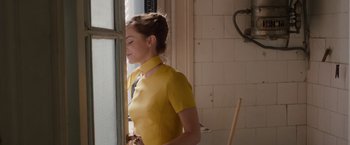 Movie still from “Colonia” (2015), directed by Florian Gallenberger – A woman in a yellow shirt looking out a window; Medium shot, Over the shoulder angle