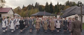 Movie still from “Colonia” (2015), directed by Florian Gallenberger – A large group of people standing in front of a house; Wide shot, High angle