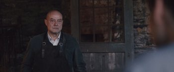 Movie still from “Colonia” (2015), directed by Florian Gallenberger – A man in a black jacket standing in front of a window; Medium shot, Low angle