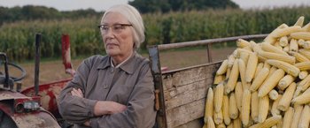 Movie still from “Colonia” (2015), directed by Florian Gallenberger – An older woman sitting on a bench in front of a corn field; Medium shot, Over the shoulder angle