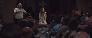 Movie still from “Colonia” (2015), directed by Florian Gallenberger – A woman sitting in front of a group of people in front of a cross; Wide shot, High angle