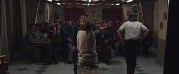 Movie still from “Colonia” (2015), directed by Florian Gallenberger – A group of people sitting in a room with a cross in the background; Wide shot, High angle