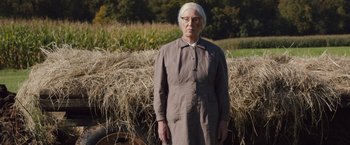 Movie still from “Colonia” (2015), directed by Florian Gallenberger – An older woman standing in front of a pile of hay; Medium shot, Low angle