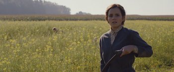 Movie still from “Colonia” (2015), directed by Florian Gallenberger – A woman standing in front of a field of yellow flowers; Medium shot, Over the shoulder angle