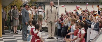 Movie still from “Colonia” (2015), directed by Florian Gallenberger – An older man in a suit stands in front of a crowd; Medium shot, Low angle
