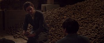 Movie still from “Colonia” (2015), directed by Florian Gallenberger – A woman sitting on the ground in front of a pile of potatoes; Medium shot, Over the shoulder angle