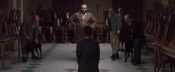 Movie still from “Colonia” (2015), directed by Florian Gallenberger – A group of people standing in a room with chairs in the background; Wide shot, Low angle