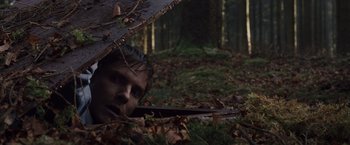 Movie still from “Colonia” (2015), directed by Florian Gallenberger – A man hiding under an umbrella in the woods; Wide shot, High angle