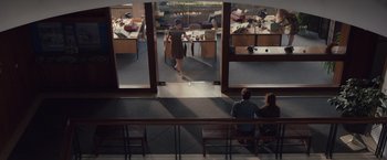 Movie still from “Colonia” (2015), directed by Florian Gallenberger – Two people sitting in a room and a woman walking in front of a desk; Extreme Wide shot, High angle