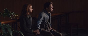 Movie still from “Colonia” (2015), directed by Florian Gallenberger – A man and a woman holding hands while sitting on top of a bench; Medium shot, Low angle