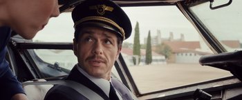 Movie still from “Colonia” (2015), directed by Florian Gallenberger – A man wearing a hat sitting in the driver's seat of a car; Close Up shot, Low angle