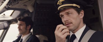 Movie still from “Colonia” (2015), directed by Florian Gallenberger – A man wearing a hat and a tie; Close Up shot, Low angle