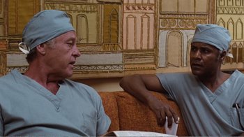 Movie still from “Coma” (1978), directed by Michael Crichton – Two doctors are sitting on a couch talking to each other; Medium shot, Low angle