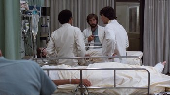 Movie still from “Coma” (1978), directed by Michael Crichton – A group of men in white lab coats standing next to a bed; Medium shot, Over the shoulder angle