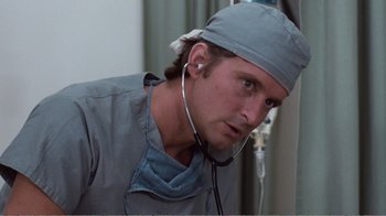 Movie still from “Coma” (1978), directed by Michael Crichton – A man wearing a surgical cap and stethoscope; Close Up shot, Low angle