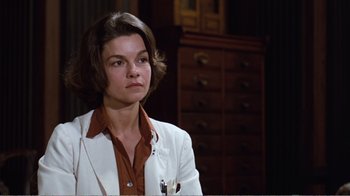 Movie still from “Coma” (1978), directed by Michael Crichton – A woman wearing a white jacket sitting in front of a wooden cabinet; Close Up shot, Low angle
