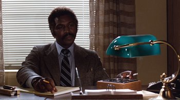 Movie still from “Coma” (1978), directed by Michael Crichton – A man sitting at a desk writing on a notebook; Medium shot, Low angle