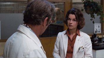 Movie still from “Coma” (1978), directed by Michael Crichton – A man and a woman in a white suit looking at each other; Medium shot, Over the shoulder angle