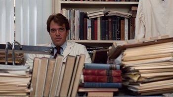 Movie still from “Coma” (1978), directed by Michael Crichton – A man sitting in front of a bookshelf filled with lots of books; Medium shot, Low angle