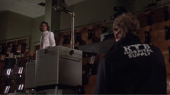 Movie still from “Coma” (1978), directed by Michael Crichton – A woman standing in front of a man in front of a camera; Wide shot, Low angle