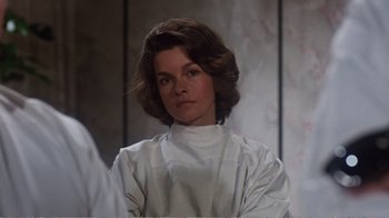 Movie still from “Coma” (1978), directed by Michael Crichton – A woman wearing a white shirt and a brown hair wig; Close Up shot, Over the shoulder angle